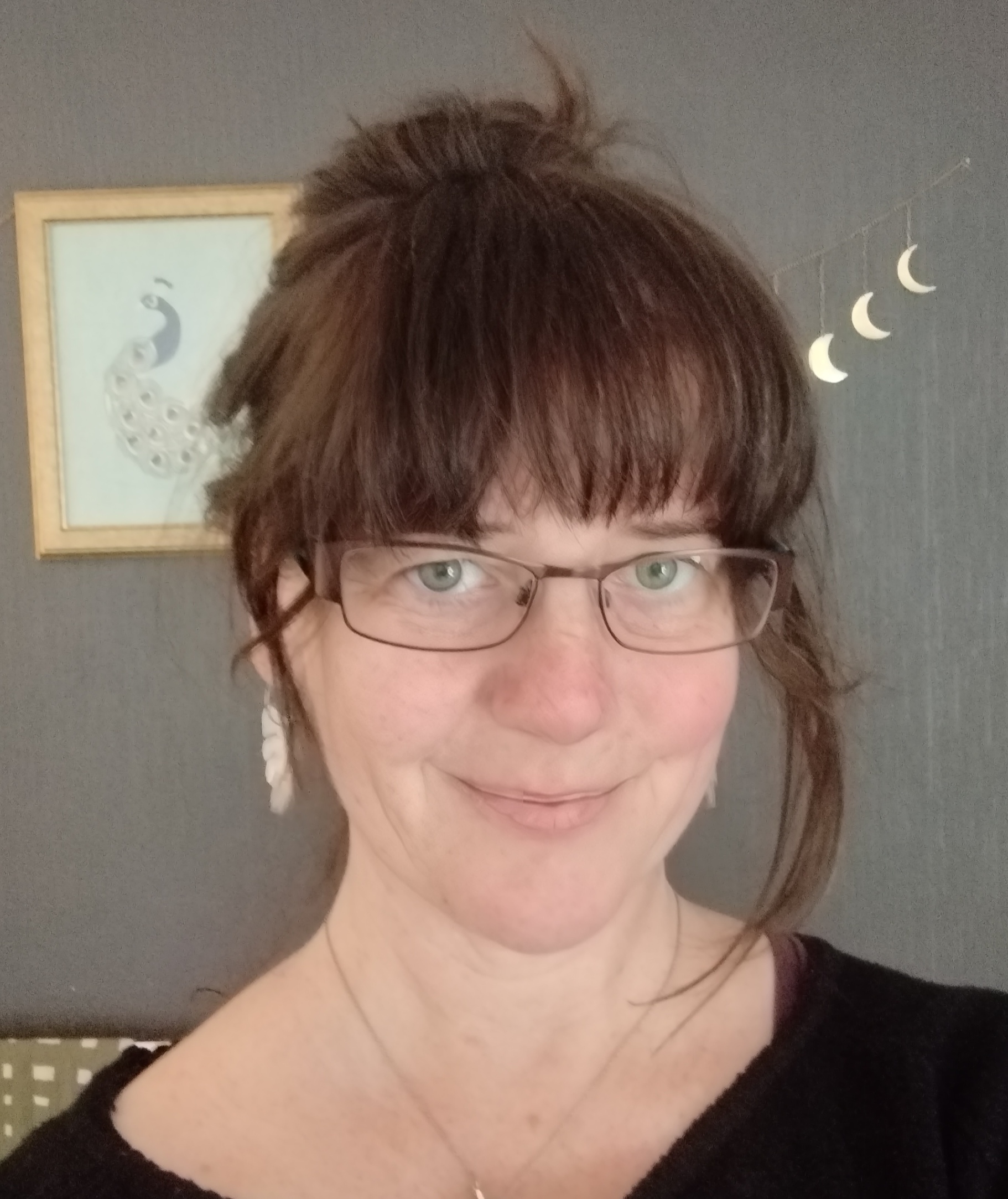 Photo of a white woman with dark hair, a big fringe and glasses, smiling. 