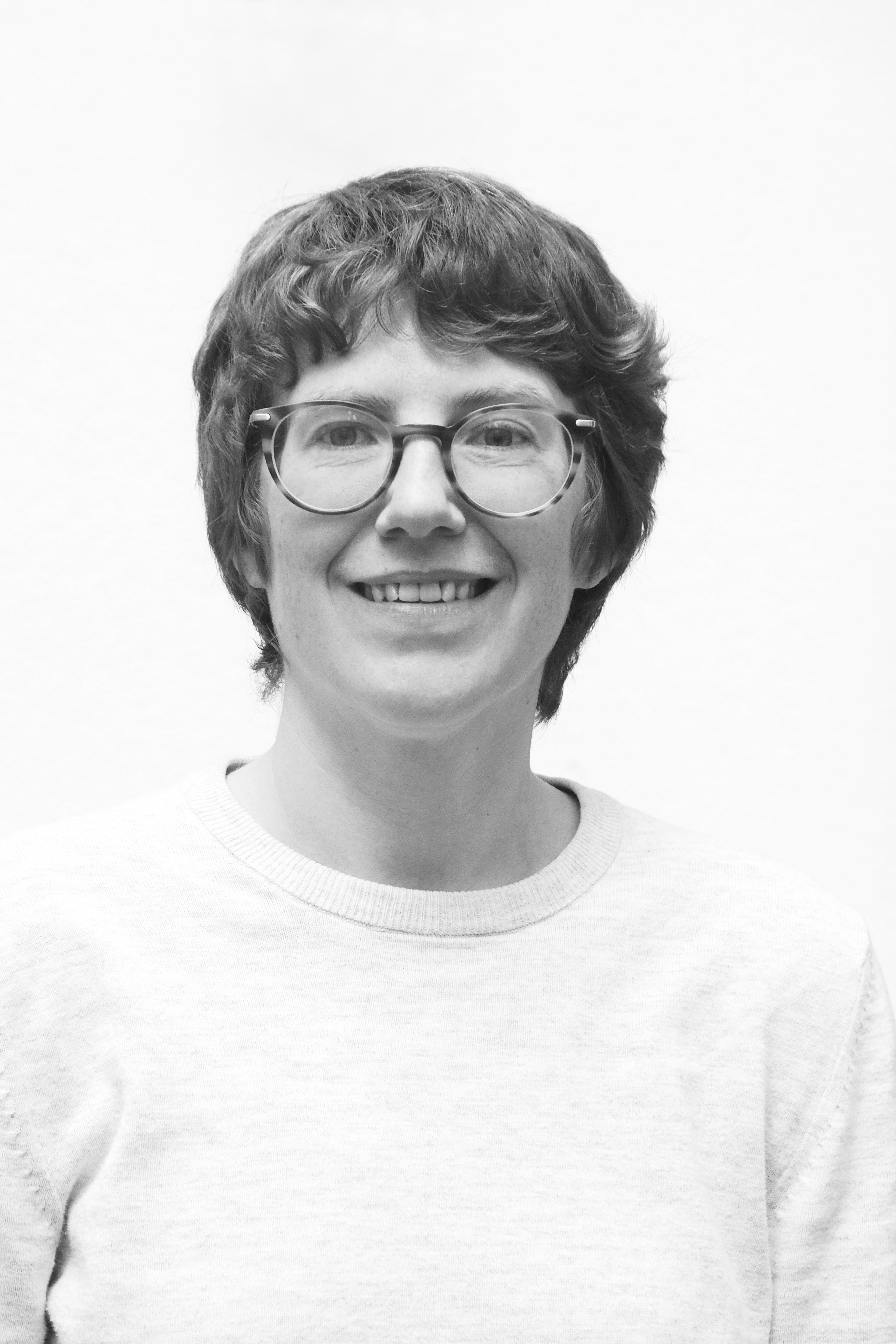 Black and white head shot of a white person with short hair and glasses, who is smiling