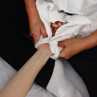 Photo of one pair of hands gently holding another hand wrapped in a white muslin cloth, stretching out the wrapped hand